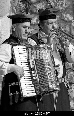 I musicisti di strada suonano l'accodiano e la tromba su una strada a Cracovia, in Polonia. I due uomini sono vestiti con abiti tradizionali polacchi. Foto Stock