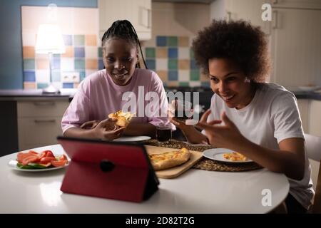 Allegre donne multietniche che condividono la pizza mentre trascorrono il tempo insieme a. a casa e chattando con gli amici online Foto Stock