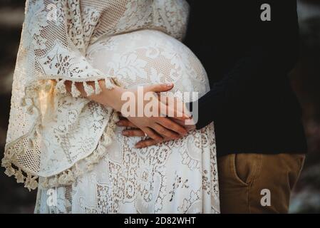 Primo piano di mani di marito e moglie incinta che toccano il ventre all'aperto Foto Stock