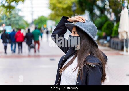 Giovane donna che indossa una maschera protettiva per il viso utilizzando lo smartphone in un città Foto Stock