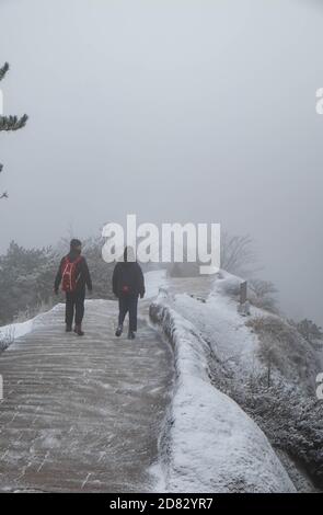 Due viaggiatori che camminano lungo la strada e molta neve coprono tutta la zona sul monte Huangshan nella stagione invernale, fa freddo. Foto Stock
