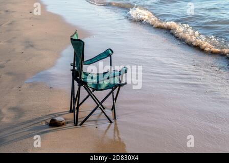 Una sedia da spiaggia pieghevole in tessuto si trova nella sabbia bagnata Lungo le rive del lago Michigan Foto Stock