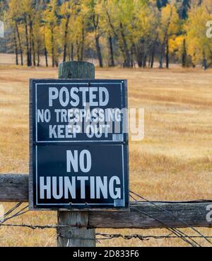 Un segno di No Hunting, No Trespassing affisso su una recinzione di filo spinato di legno in un campo di erba selvatica dorata e alberi durante la stagione di caccia con spazio di copia Foto Stock