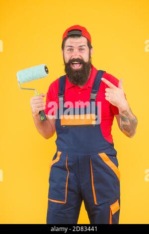 caposquadra che va fare il muro di fronte. felice uomo brutale in uniforme boilersuit. hipster maturo uso rullo di vernice strumento per la pittura. repairman o costruttore di lavoro. idea creativa. Foto Stock