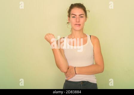 Studio shot della bella ragazza adolescente di mordere il suo labbro con il pugno alzato contro verde parete dipinta Foto Stock