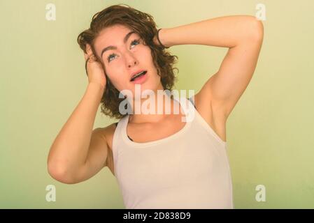 Studio shot della bella ragazza adolescente pensare con entrambe le mani sulla testa contro verde parete dipinta Foto Stock