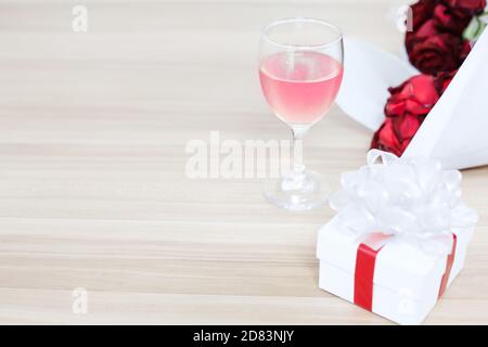 Bicchiere di vino messo sul tavolo di legno con un regalo e rosa rossa, concetto di felicità nel dare e ricevere doni da qualcuno speciale. Foto Stock