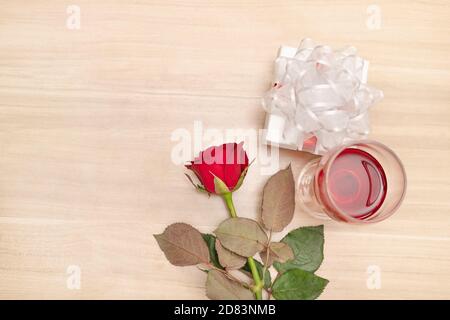 Regalo e rosa rossa da mettere sul tavolo di legno con un bicchiere di vino, concetto di felicità nel dare e ricevere doni da qualcuno speciale. Foto Stock