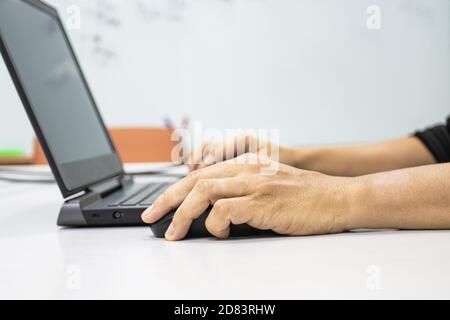 Un uomo seduto con un computer portatile con una mano per tenere un mouse mostra il concetto di sindrome da ufficio con polso weire da tenere premuto il mouse Foto Stock
