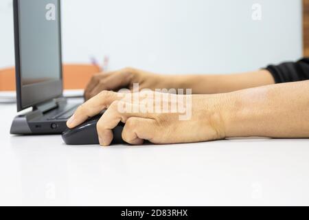 Un uomo seduto con un computer portatile con una mano per tenere un mouse mostra il concetto di sindrome da ufficio con polso weire da tenere premuto il mouse Foto Stock