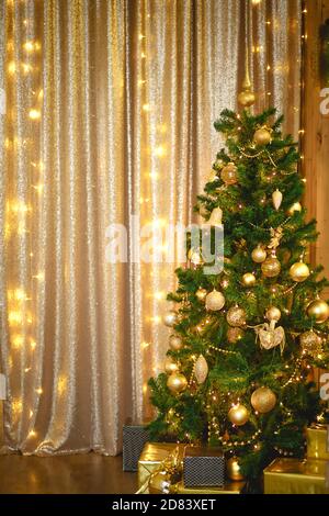 Abete bianco artificiale verde Natale nella sala d'Oro con luci garlands decorate con palline d'oro, perle e giocattoli. La scatola con i regali in foi Foto Stock