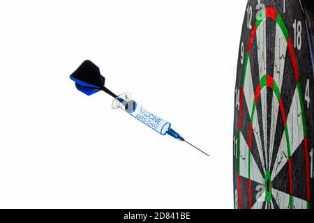 Una siringa monouso sotto forma di una freccetta con l'iscrizione del vaccino vola in un bersaglio della tavola da disegno, isolato su uno sfondo bianco. Coronavirus Foto Stock