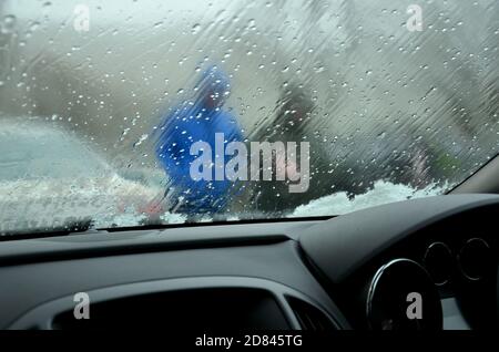 primo piano del parabrezza dell'auto con la neve sopra e il cruscotto. guardando attraverso il parabrezza con le gocce di pioggia a persone auto davanti Foto Stock