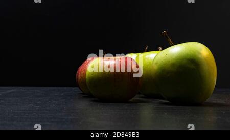 Tre mele verdi fresche mature e due mele rosse su tavola nera e sfondo scuro. Spazio libero per la copia. Spuntini scolastici o concetto di cibo biologico Foto Stock