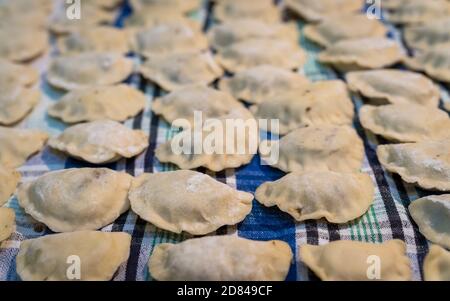 Cibo tradizionale polacco chiamato pierogi, simile ai ravioli italiani, appena arrotolati in pasta e asciugati sul tavolo da cucina, pronti per essere cotti Foto Stock