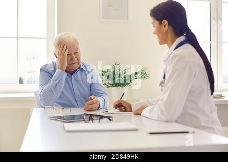 Paziente anziano che si lamenta di mal di testa alla giovane donna positiva medico Foto Stock