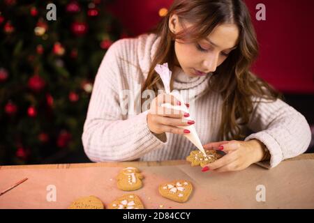 Concetto tradizionalista. Bruna carina giovane donna glassare pan di zenzero di Natale Foto Stock