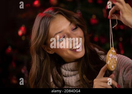 Concetto tradizionalista. Simpatica giovane donna gioca con i biscotti di Natale decorati Foto Stock