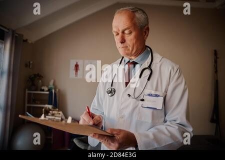 Il medico di sesso maschile scrive le note sulla clipboard in ospedale Foto Stock
