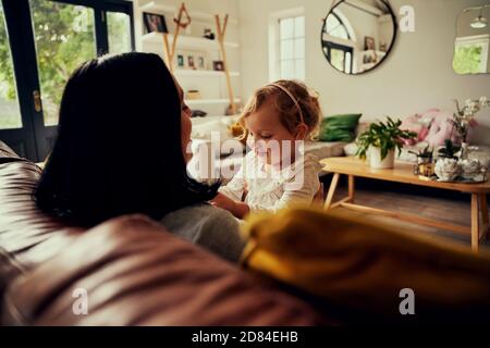 Felice giovane madre seduta sul divano sorridente e giocando con il bambino in soggiorno Foto Stock