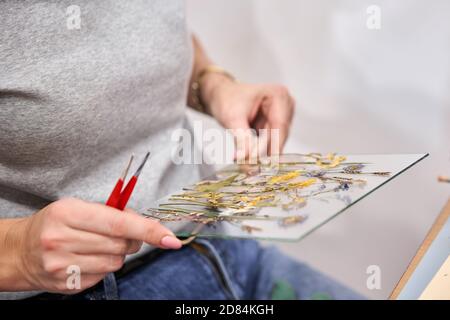 Una donna presenta una composizione. Master class sulla creazione di cornici con Herbarium in tecnica tiffany in vetro colorato. Erbario di diverso essiccato Foto Stock