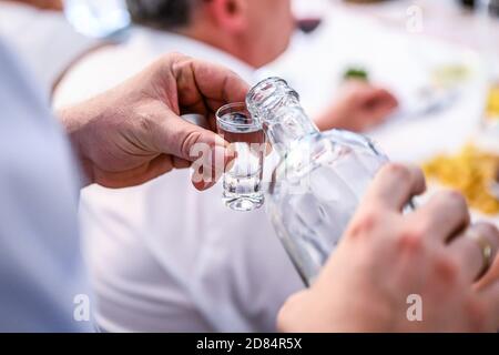 Mano con una bottiglia di Vodka versata in un bicchiere isolato durante un matrimonio di festa. Foto Stock