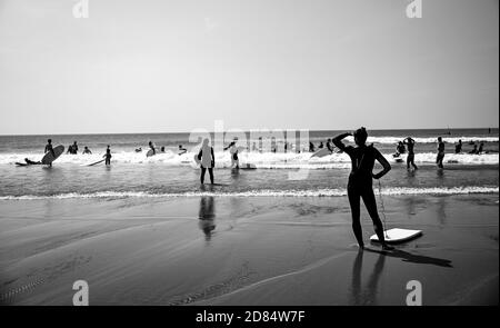 Immagine monocromatica di Surfers giocare ai margini della spiaggia in bianco e nero in mute a Croyde Bay, Devon Foto Stock