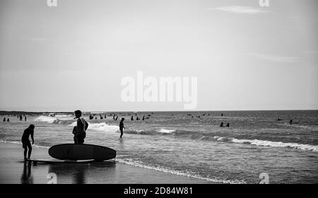 Immagine monocromatica di Surfers giocare ai margini della spiaggia in bianco e nero in mute a Croyde Bay, Devon Foto Stock