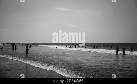 Immagine monocromatica di Surfers giocare ai margini della spiaggia in bianco e nero in mute a Croyde Bay, Devon Foto Stock