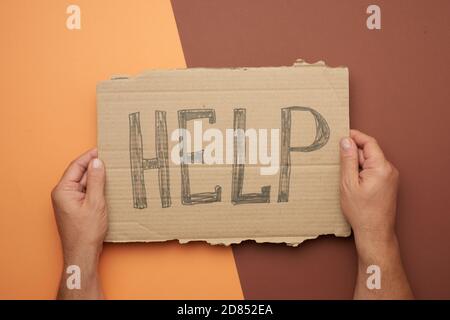 la mano maschile tiene un pezzo di cartone con l'iscrizione aiuto, il concetto di mutua assistenza, senza tetto, crisi finanziaria Foto Stock