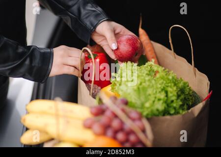 Primo piano di generi alimentari in pacchetto eco nel bagagliaio dell'auto. Mani di donne che imballano le verdure e la frutta dopo la spedizione in supermercato Foto Stock