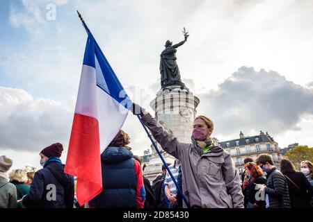 Un uomo che indossa una maschera facciale sta tenendo una bandiera francese ai piedi del Monumento alla Repubblica durante una manifestazione a Parigi, Francia. Foto Stock