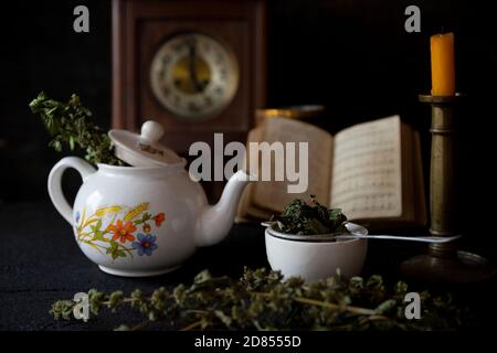 Tazza di tè e teiera su tavolo di legno con orologio vecchio, candela e libro in background Foto Stock