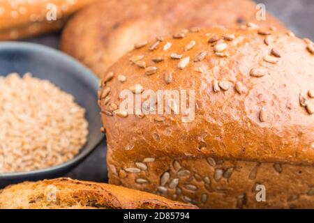 Diversi tipi di pane fresco cotto e piatto blu con grani su sfondo nero di cemento. Vista laterale, fuoco selettivo, primo piano. Foto Stock