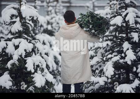 Giovane bell'uomo che porta fresco abete tagliato all'aperto Foto Stock