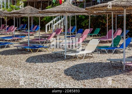 Vista sulla spiaggia vuota - lettini e ombrelloni colorati, alberi verdi e cespugli fioriti. Località estiva abbandonata. Foto Stock