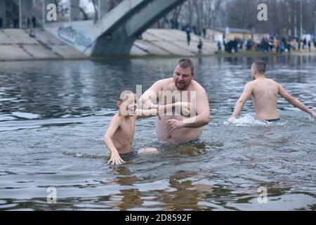 Uomo che tira il ragazzo in acqua ghiacciata per battezzare durante la festa Epifania sul fiume Dnipro. 19 gennaio 2020. Kiev, Ucraina Foto Stock