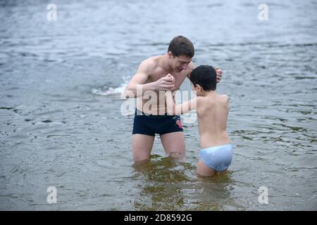 Uomo che tira il ragazzo in acqua ghiacciata per battezzare durante la festa Epifania sul fiume Dnipro. 19 gennaio 2020. Kiev, Ucraina Foto Stock