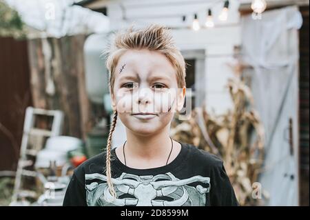 un ragazzo in un costume scheletro con una faccia dipinta sul portico di una casa decorata per celebrare un Festa di Halloween Foto Stock