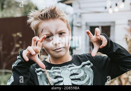 un ragazzo in un costume scheletro con una faccia dipinta sul portico di una casa decorata per celebrare un Festa di Halloween Foto Stock