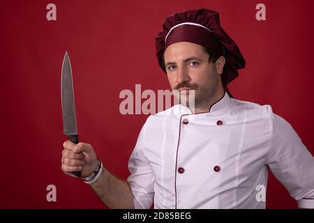 Unshaven bel cuoco maschile cuoco tenendo chef coltello guardando fotocamera Foto Stock