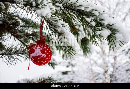 Sfondo di Natale con una palla di Natale a maglia rossa con cervi sul ramo di pino innevato nella foresta invernale con spazio di copia. Festa di nuovo anno, Chris Foto Stock