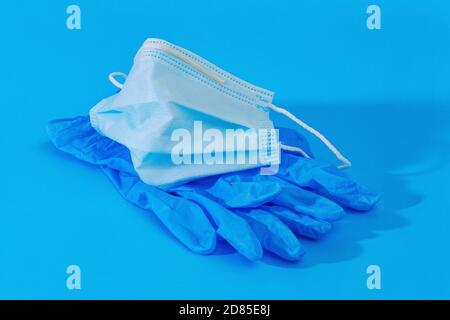 paio di guanti medici blu e maschera medica viso su sfondo blu Foto Stock