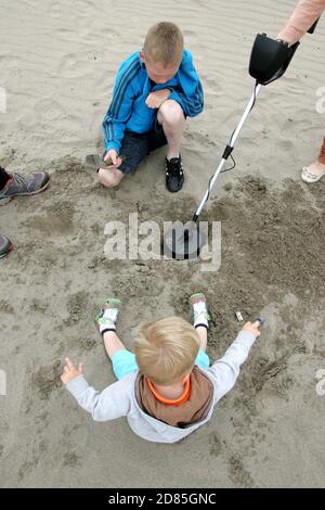 Girvan, Ayrshire, Scozia, Regno Unito. Una famiglia sulla spiaggia metal detecting in cerca di tesoro, sullo sfondo può essere visto l'iconica Ailsa Craig Foto Stock