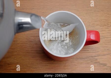 preparare una tazza di tè, versando acqua calda sopra il teabag in tazza rossa, norfolk, inghilterra Foto Stock