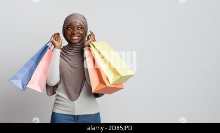 Felice donna shopaholic musulmana nera in hijab che posa con lotti borse per acquirenti Foto Stock