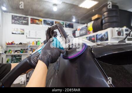 Il master in stazione di servizio lucida la carrozzeria di auto, utilizzando una macchina lucidatrice, lucido, pulire, coperte di cera, cappa nera dopo la verniciatura e washin Foto Stock