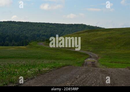 Strada di campagna attraverso un grande pascolo o prato che si snoda intorno ad una collina in distanza. Foto Stock