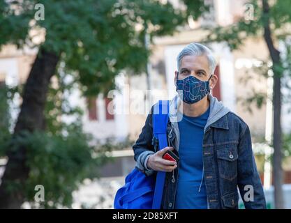 Bel maschio cubano che indossa una maschera protettiva che cammina lungo la strada dentro Madrid e guardare via mentre si gode una passeggiata nel fine settimana durante il coronavirus epidemia Foto Stock