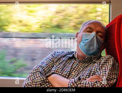 Uomo che indossa la maschera che dorme sul treno Foto Stock